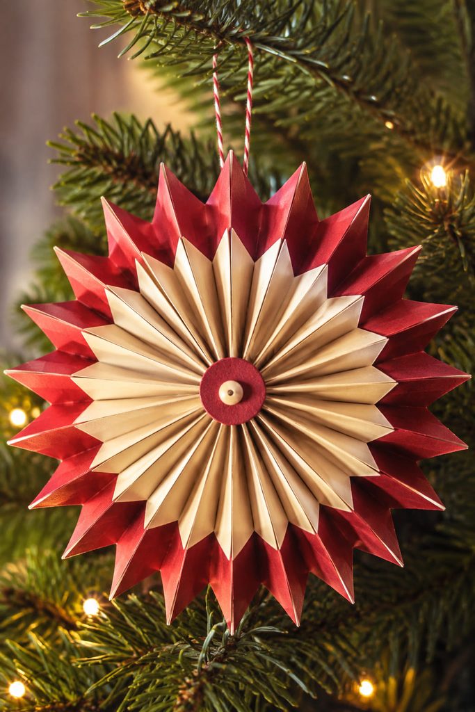 Paper Christmas ornaments featuring an accordion-fold star hanging among evergreen branches.