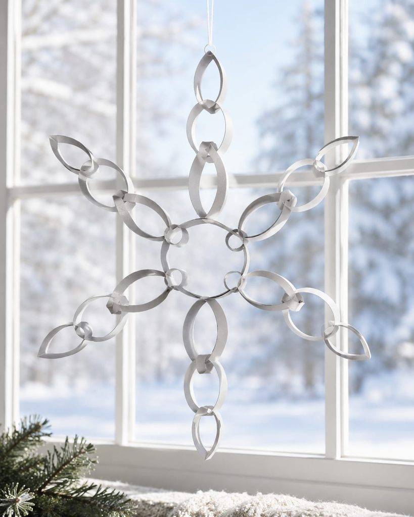 Six-arm snowflake made from linked paper loops hanging against a bright window.