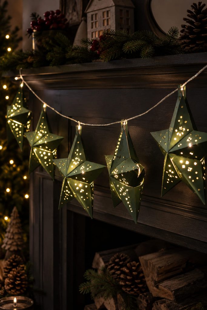 Hollow folded paper stars glowing from cool micro-LEDs along a Christmas mantel.