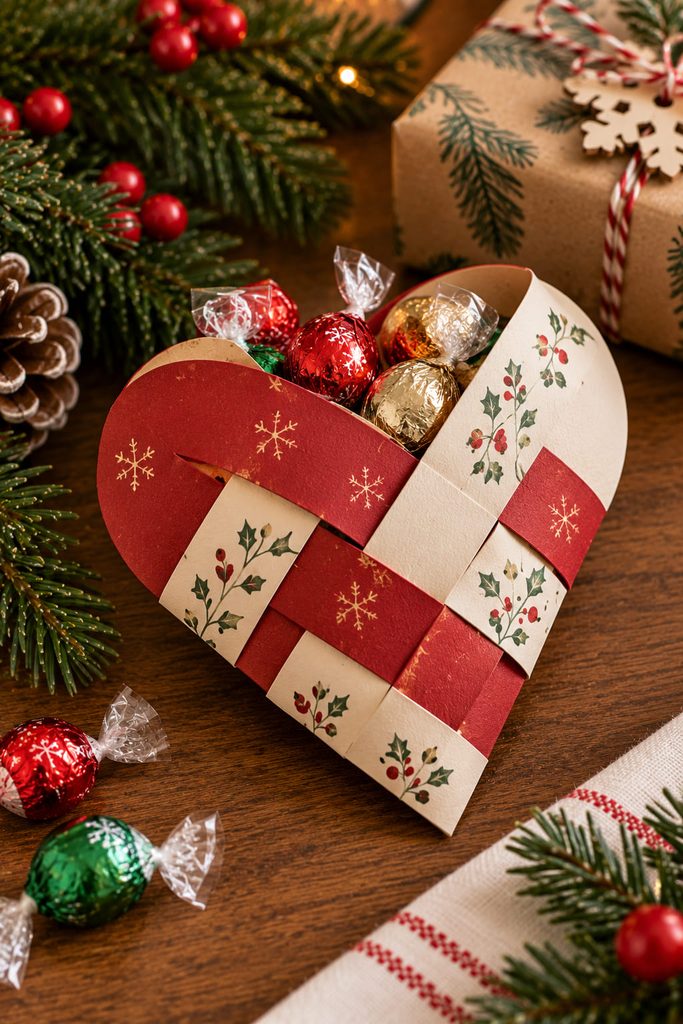 Red and cream woven paper heart pocket holding small wrapped Christmas treats.